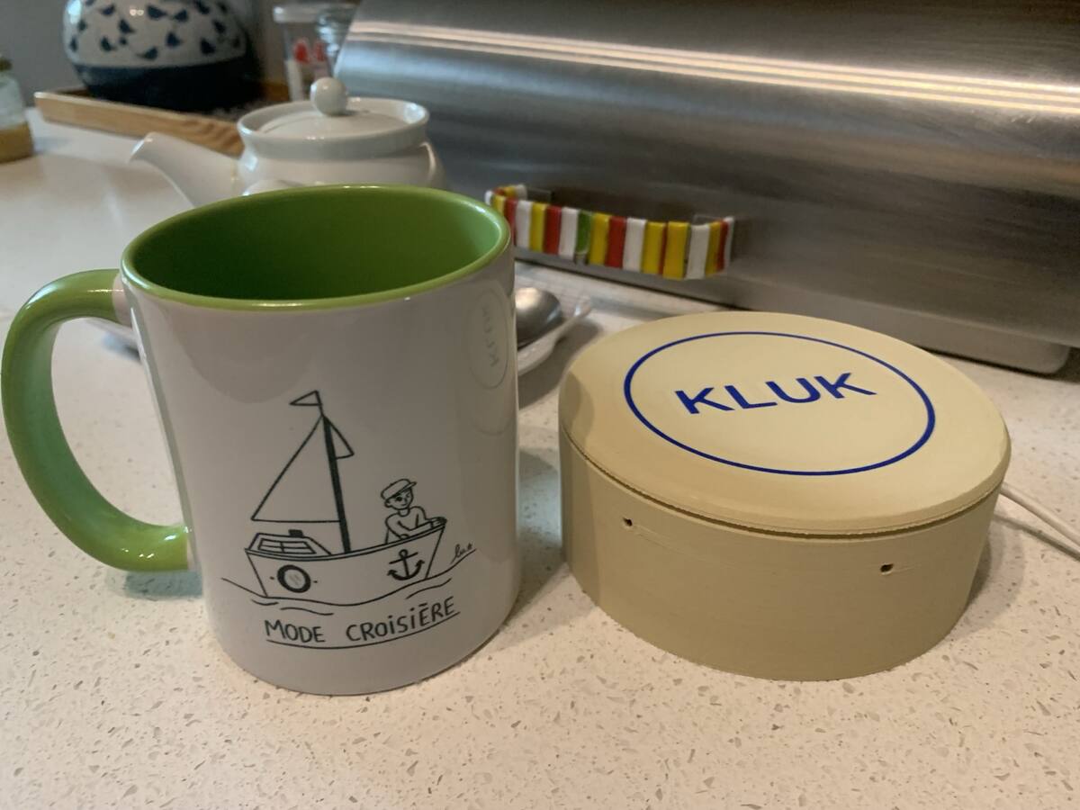 La Kluk, un socle rond beige marqué « KLUK » en bleu, posée à côté de la tasse « Mode croisière ».